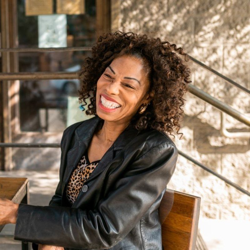 Woman with curly hair laughing at an outdoor cafe